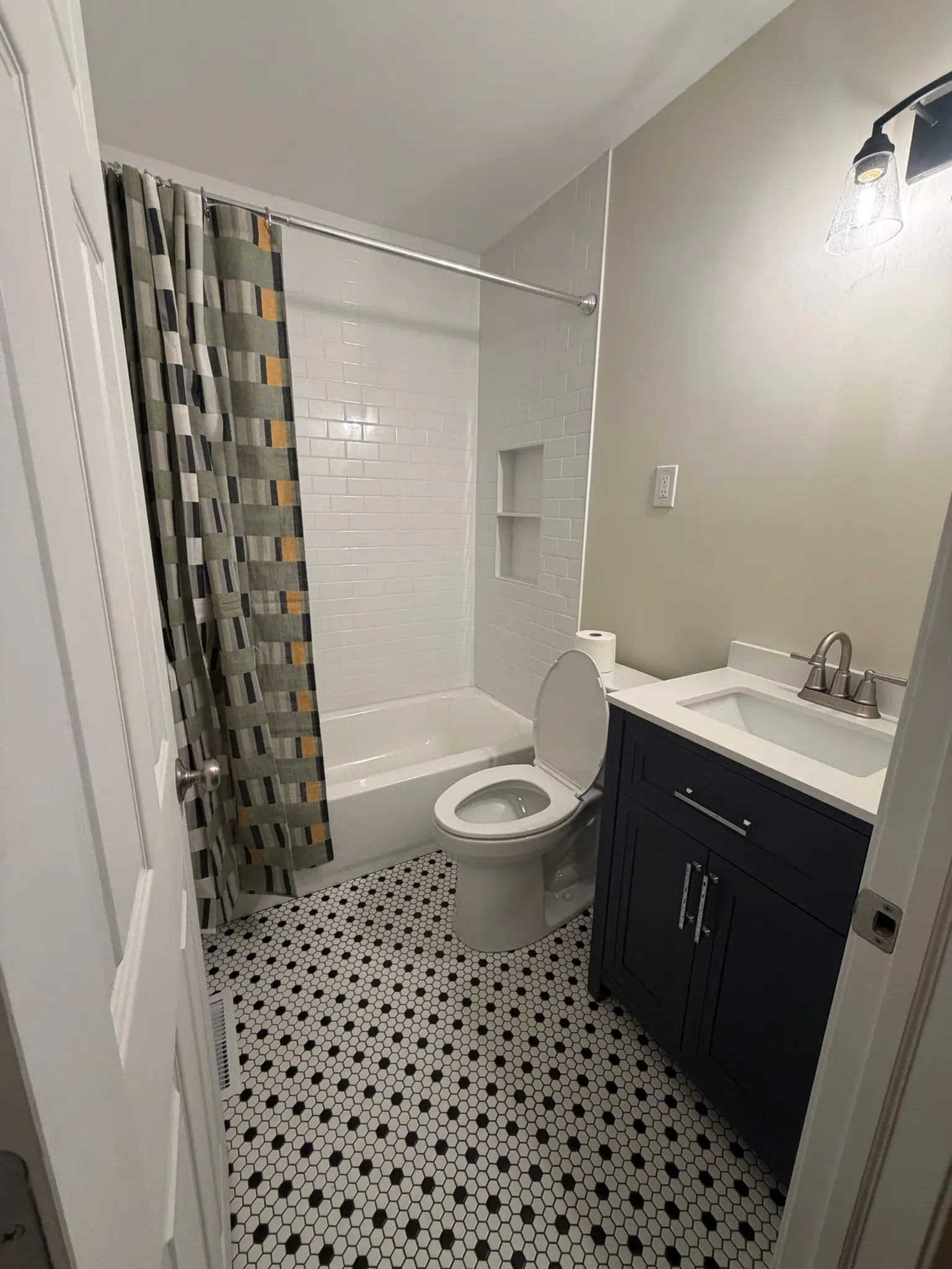 Remodeled bathroom with navy vanity, white subway tile and hex floor tile