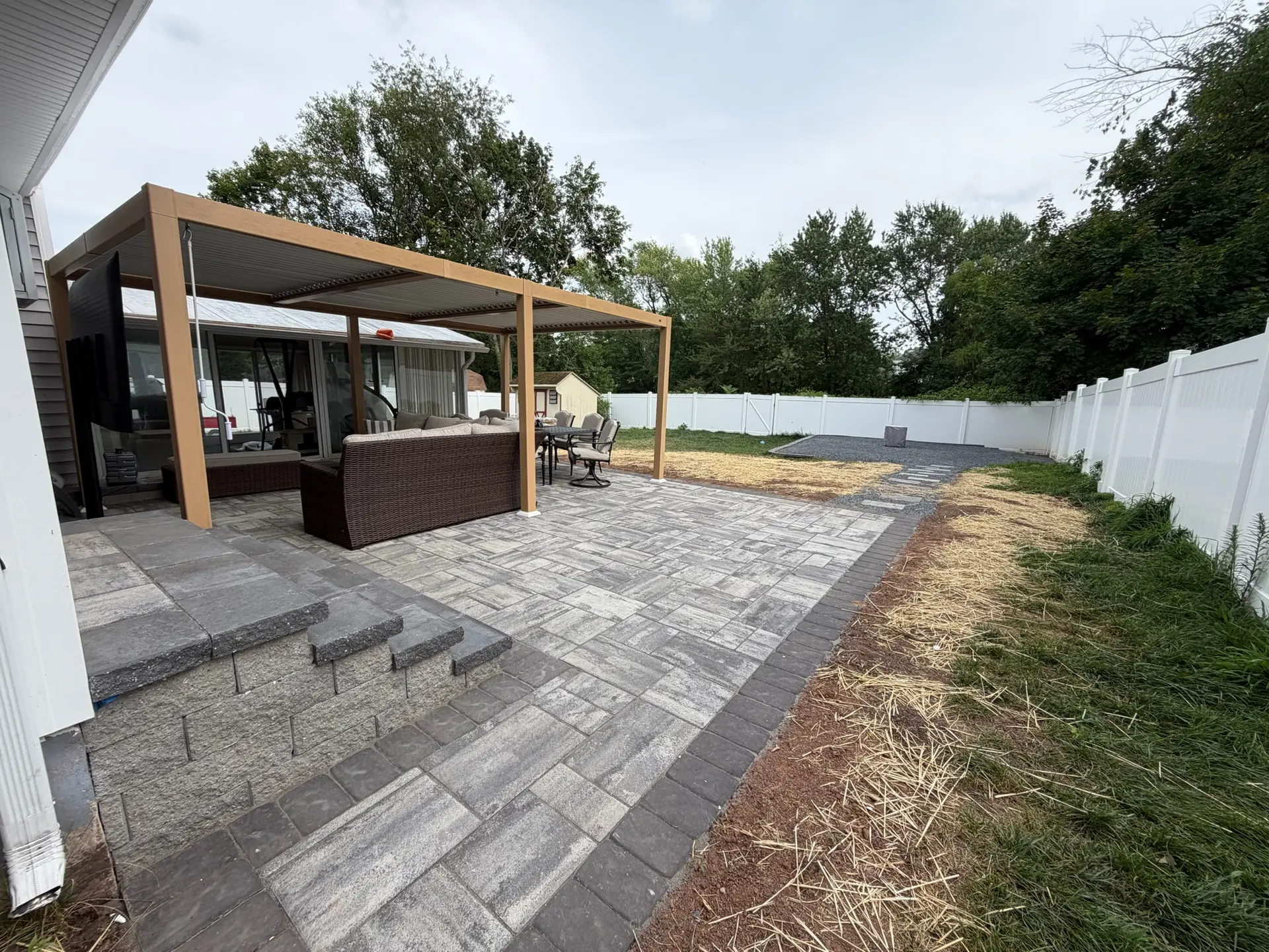 Paver patio with a wooden pergola and outdoor seating behind a home