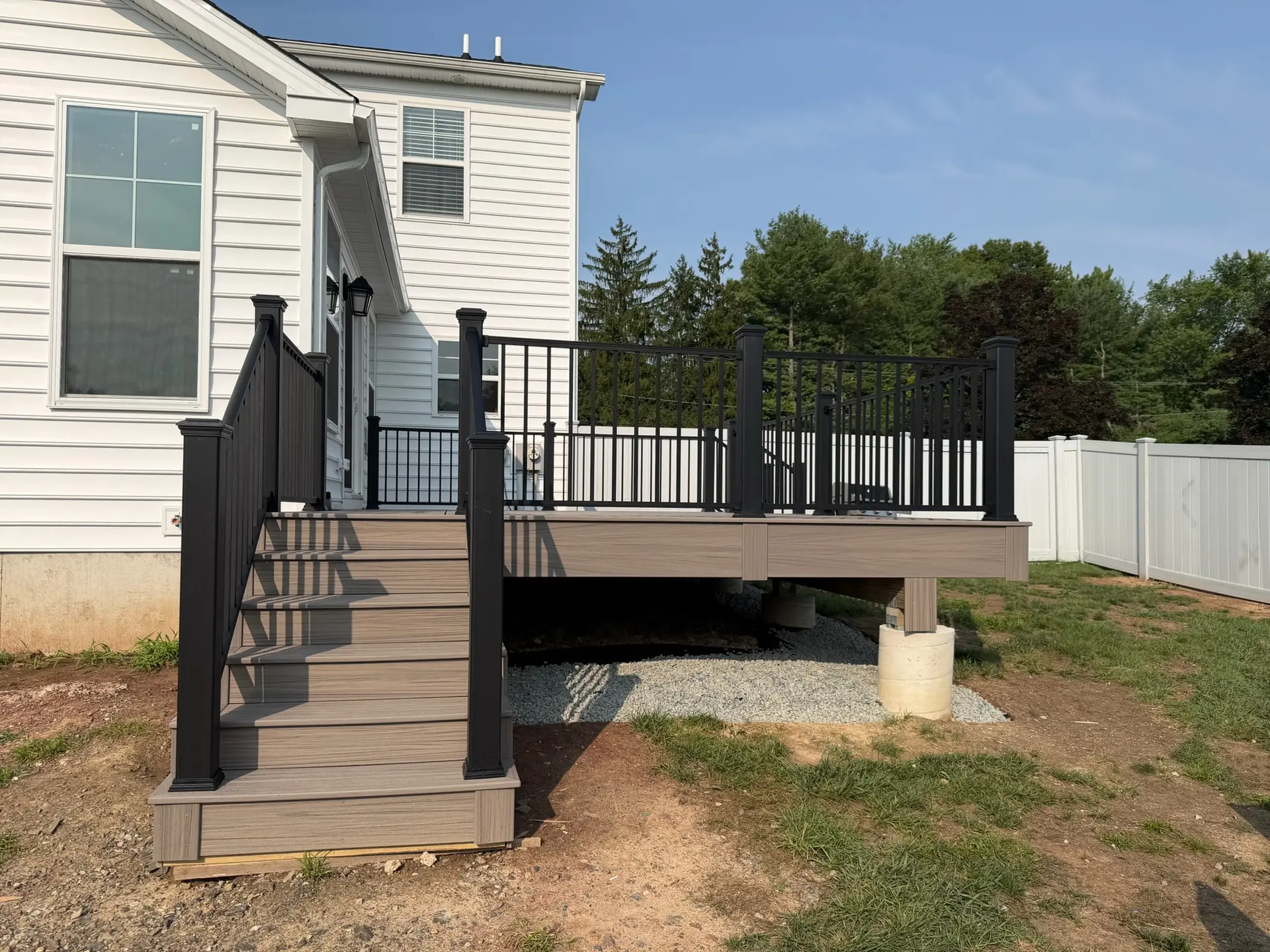 Composite deck stairs with black railing and posts beside a white vinyl sided home