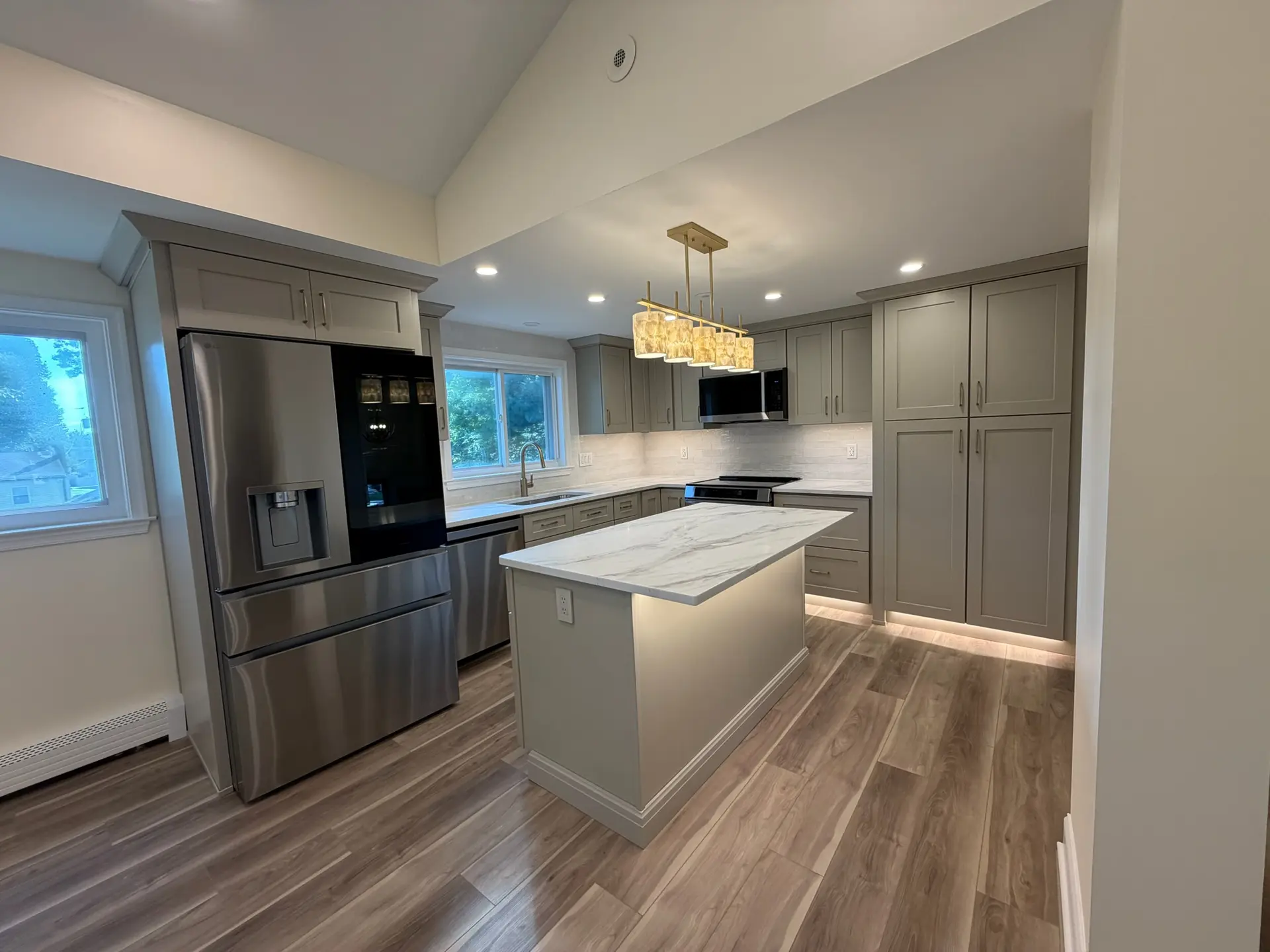 A newly remodeled kitchen with sage green cabinets, a quartz island and brass pendant lighting
