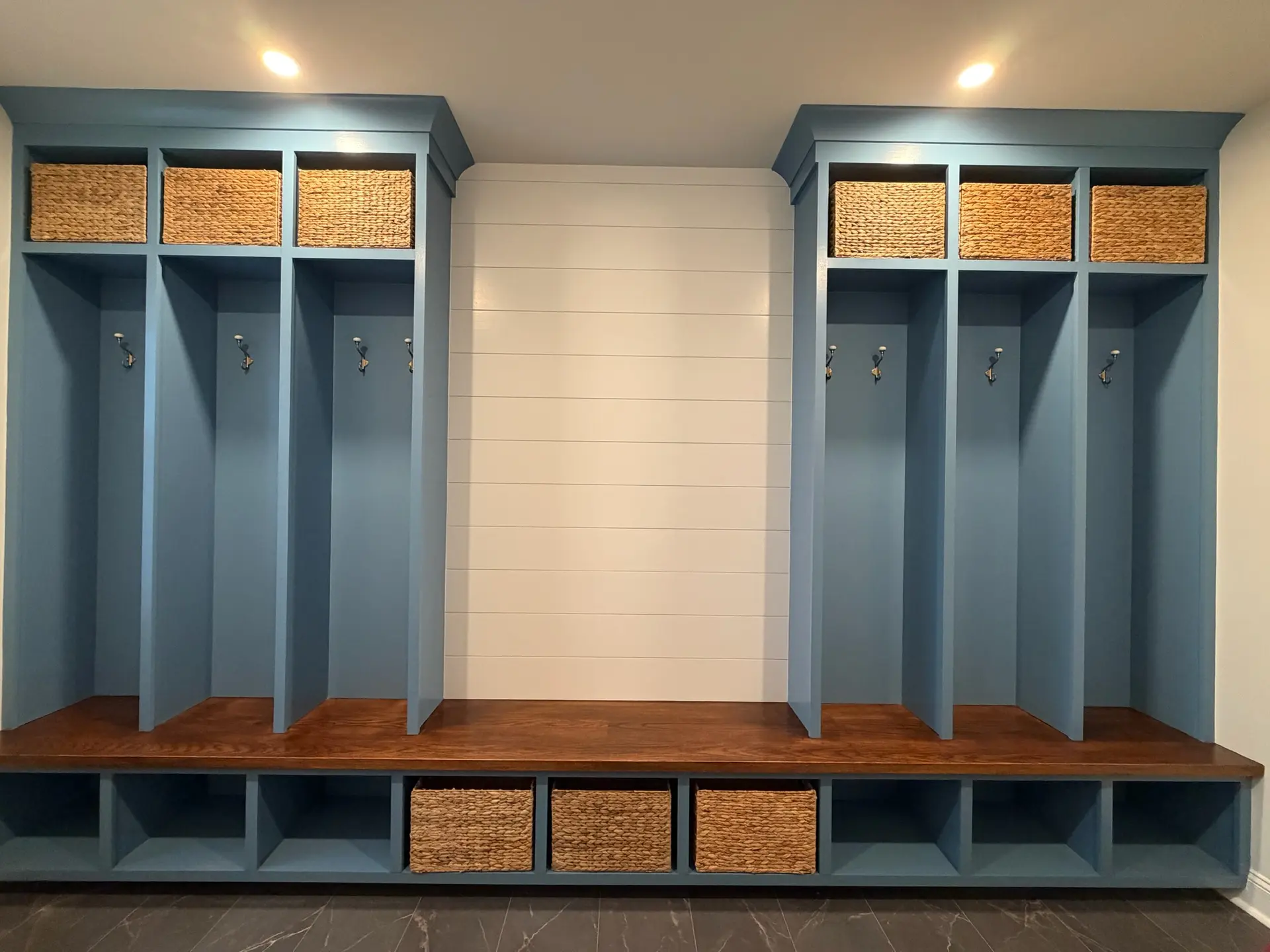 Custom blue mudroom cubbies with wicker baskets, shiplap wall and a stained wood bench
