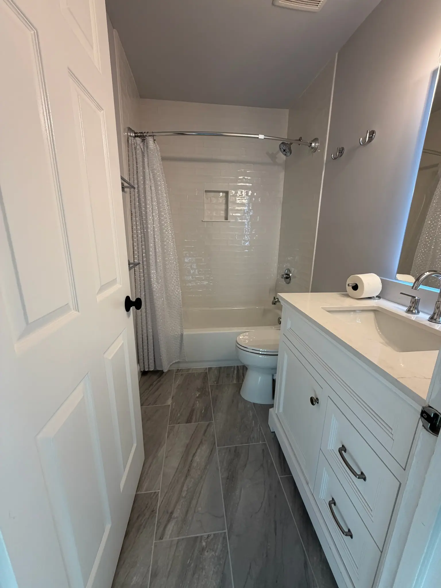 Bathroom remodel with white vanity, subway tile tub and large format gray floor tile