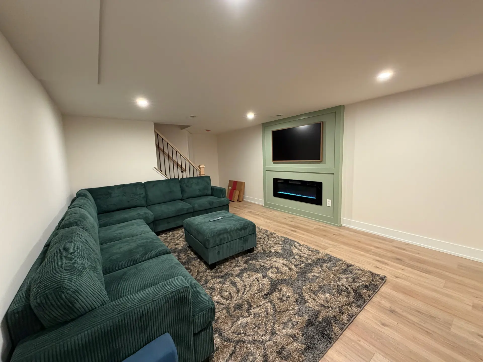Finished basement with green sectional, built-in media wall and electric fireplace